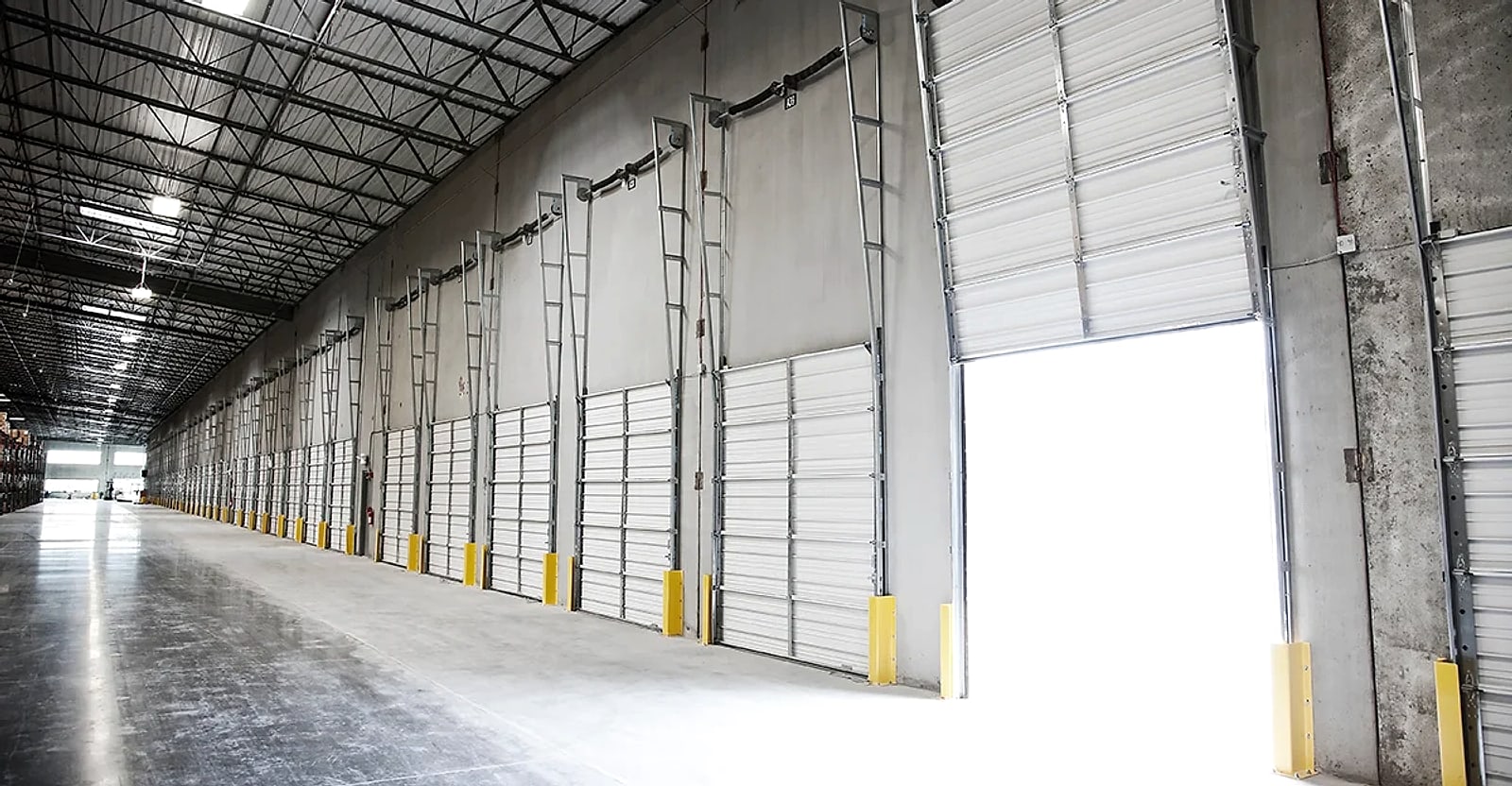 Interior of a shallow-bay industrial warehouse with a long row of loading dock doors